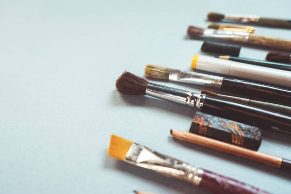 на голубой поверхности находятся художественные кисти разных размеров, карандаши и ручки
