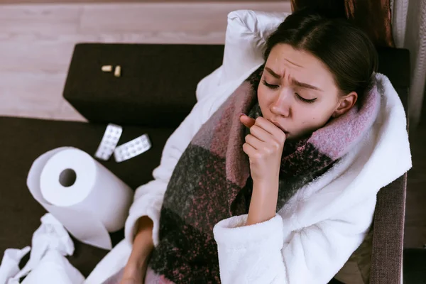 sad young girl gets sick, sore throat, coughs, neck warm scarf, next to lie pill for cold