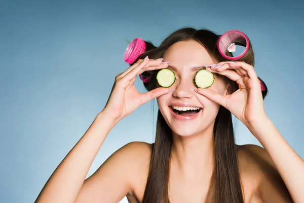 Curlers başkanı yüzünde Cilt nemlendirici için salatalık parçalarını tutarak gülünecek bir genç kız — Stok fotoğraf