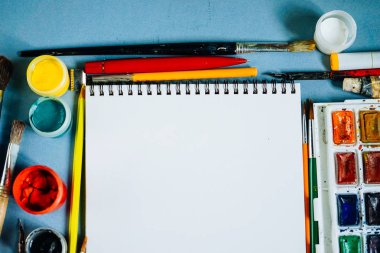 mavi bir masada yalan sanat malzemeleri, resim kağıdı, suluboya ve guaş, fırçalar