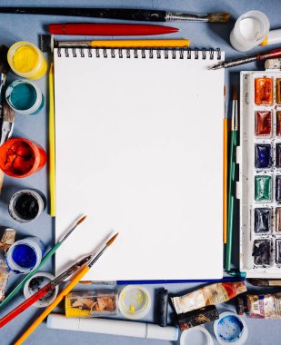 mavi bir masada yalan sanat malzemeleri, resim kağıdı, suluboya ve guaş, fırçalar