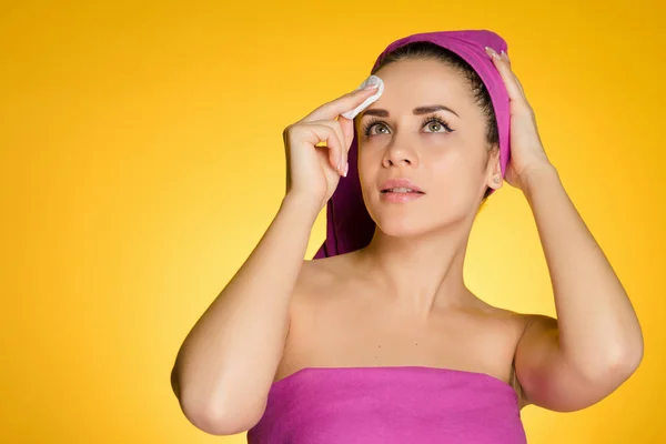 Красивая молодая девушка с розовым полотенцем на голове очищает кожу на лице с помощью хлопкового диска — стоковое фото