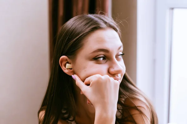 Ein junges Mädchen blickt nachdenklich aus dem Fenster, in den Ohren gelbe Ohrstöpsel gegen den Lärm — Stockfoto