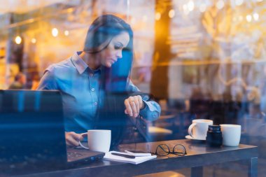 esmer kız serbest meslek sahibi bir kol saati görünümlü bir dizüstü bilgisayarda bir kafede çalışıyor
