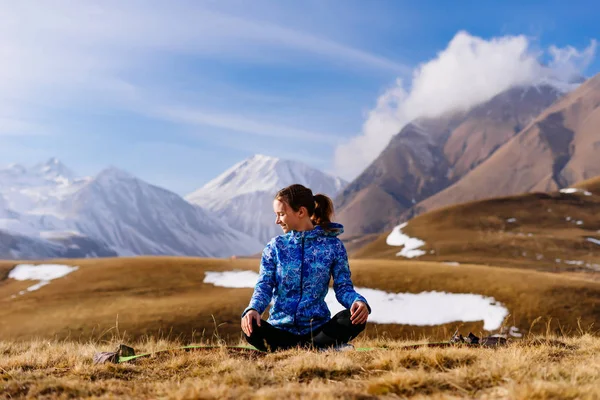 Активная девушка занимается йогой и ведет здоровый образ жизни, наслаждается природой и Кавказскими горами, сидит на земле — стоковое фото
