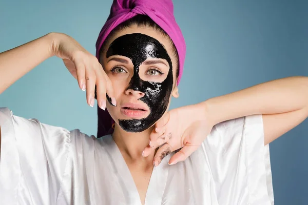 Bela jovem com uma toalha rosa na cabeça, em seu rosto uma máscara de limpeza preta — Fotografia de Stock
