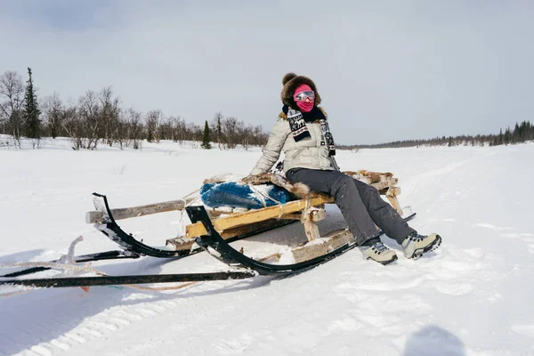 En flicka i varma kläder reser norrut, sitter på släden, runt om snowen — Stockfoto