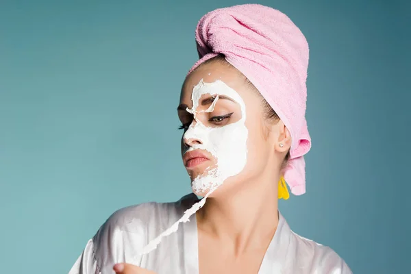 Uma jovem com uma toalha rosa na cabeça remove uma máscara branca do rosto — Fotografia de Stock