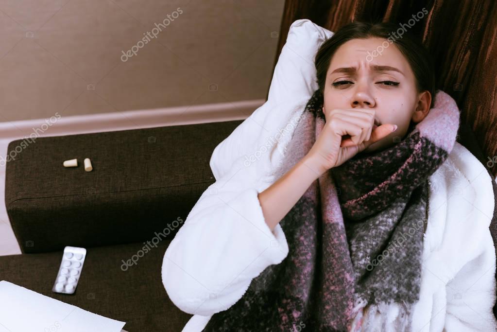 sad young girl fell ill with sore throat because of cold weather, a warm scar around her neck, coughs