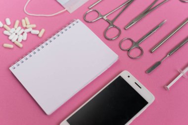 pembe yüzeyde bir akıllı telefon, beyaz hap, defter ve diş aletleri olduğunu