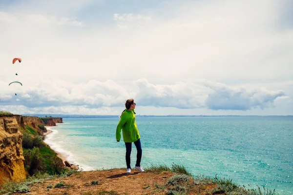 Ragazza in giacca verde gode della natura, guarda il mare — Foto Stock