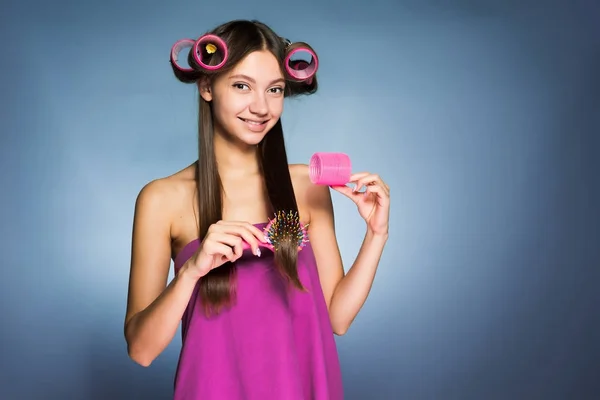 Bela menina sorridente quer fazer um belo penteado, na cabeça de um curler, mantém um pente na mão — Fotografia de Stock