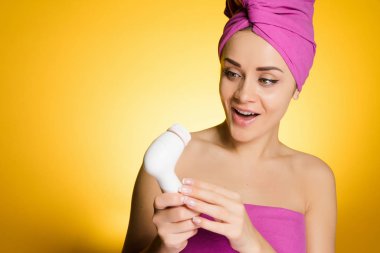 sürpriz güzel kız kafasına sarı bir arka plan üzerinde pembe bir havlu ile özel bir fırça ile yüzündeki derinin derin bir temizlik yapar