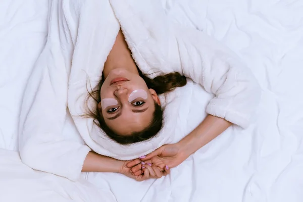 화이트 테리 드레싱 가운에서 젊은 아름 다운 소녀 실리콘 패치 눈 아래 침대에 누워 — 스톡 사진