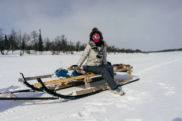 En flicka i varma vinterkläder reser norrut, sitter på en släde, en snötäckt väg — Stockfoto