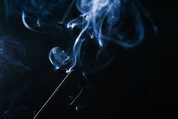 Sobre un fondo negro palillo aromático ardiente, humo azul — Foto de Stock