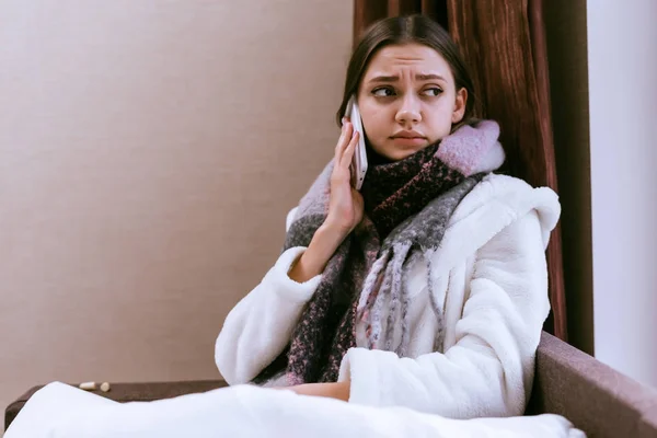 Sad young girl is very sick because of the cold winter weather, a warm scarf around her neck, calls the hospital — Stock Photo, Image