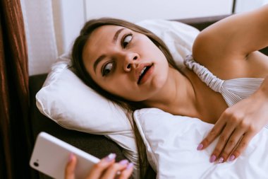 genç kız yatakta yatıyor, saat uyumuşum telefon üzerinde görünüyor