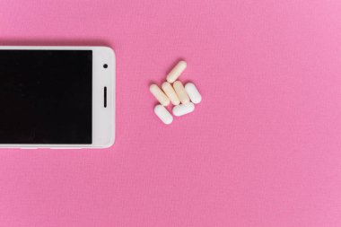 pembe bir yüzey üzerinde beyaz bir akıllı telefon ve tabletler yatıyor