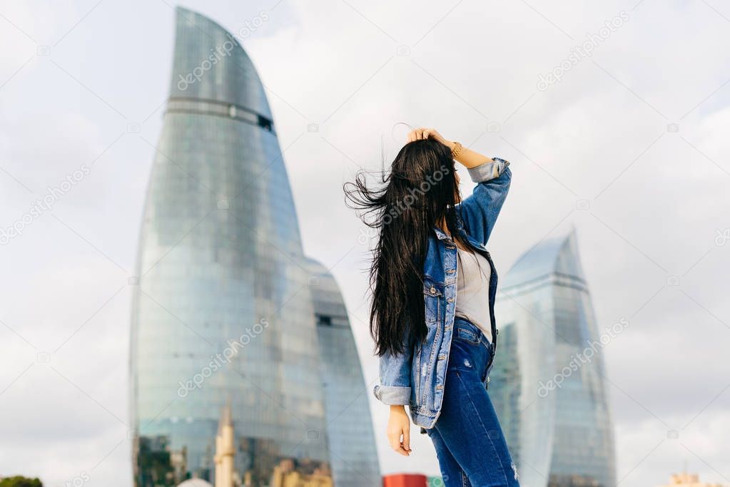 long-haired attractive girl travels through Europe on vacation, poses against the background of modern buildings in Baku