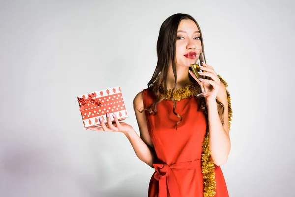 Krásná mladá dívka v červených šatech slaví Nový rok, šampaňské a drží dárek — Stock fotografie