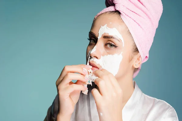 Egy fiatal lány, a fején rózsaszín törülközővel eltávolítja a fehér maszk tisztító arcán — Stock Fotó