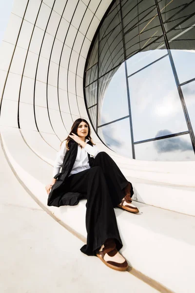 Confident stylish woman in a black suit and white shirt posing against the background of an unusual building in the city of Baku — Stock Photo, Image