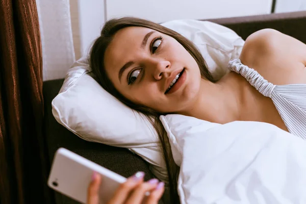 Gadis muda berbaring di tempat tidur, mematikan alarm di telepon — Stok Foto