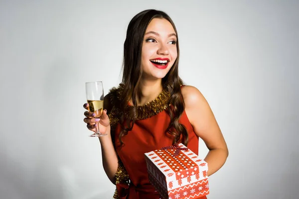 Щаслива красива дівчина з червоною помадою відзначає новий рік, тримаючи келих з шампанським і подарунком — стокове фото