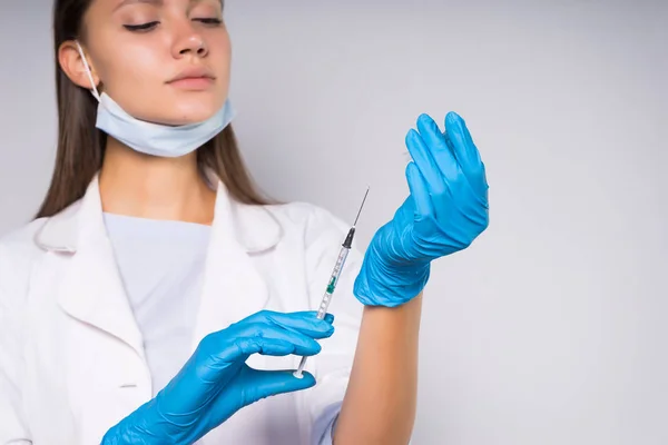 Jovem médico inteligente em vestido de vestir médico branco e luvas azuis segura uma seringa nas mãos — Fotografia de Stock