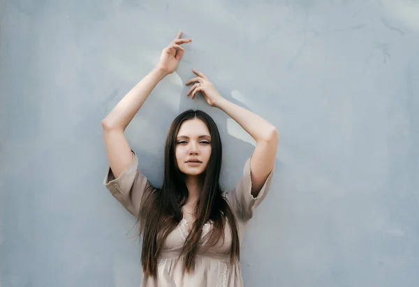 Bela sexy modelo menina de cabelos longos em vestido bege posando contra fundo de parede leve, mãos levantadas para cima — Fotografia de Stock