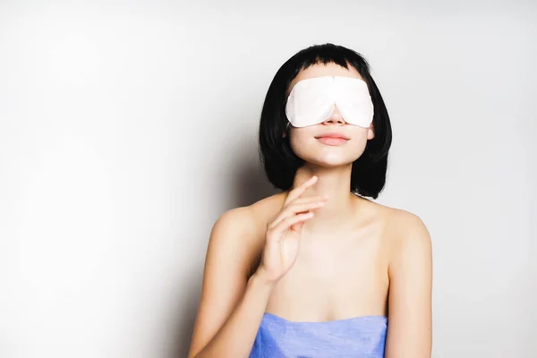Muchacha joven con el pelo corto negro en una toalla azul, delante de una máscara blanca —  Fotos de Stock