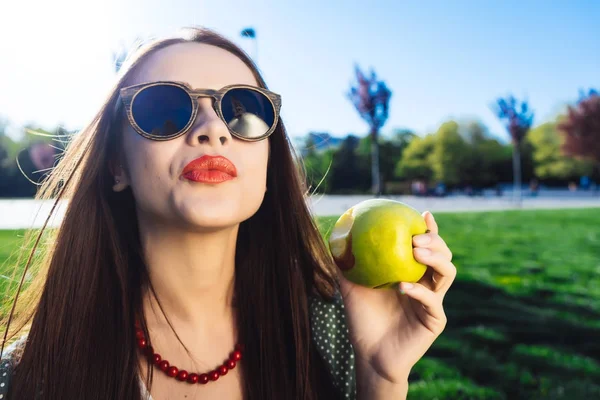 Mujer de moda en gafas, estrictas frutas de la dieta, se sienta en la hierba verde en el parque — Foto de Stock