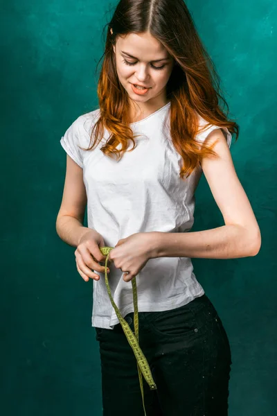 Bela menina ruiva em uma camiseta branca mede o volume de sua cintura — Fotografia de Stock