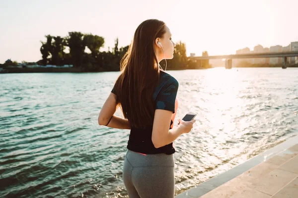 Långhårig vacker flicka jogga vid floden, lyssna på musik i hörlurar — Stockfoto