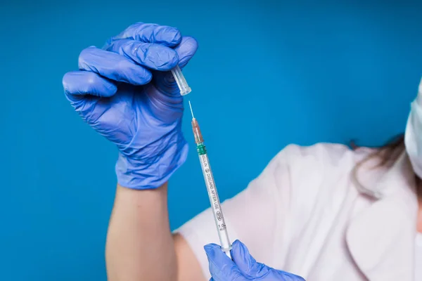 Una doctora con una bata blanca de laboratorio y guantes médicos azules sostiene una jeringa de inyecciones — Foto de Stock