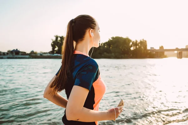 Långhåriga atletisk flicka leder en hälsosam livsstil, går längs floden vid solnedgången — Stockfoto