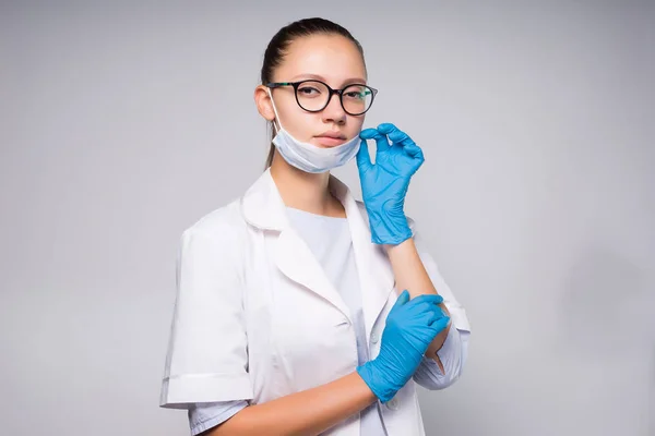 Ung allvarlig kvinna läkare bär vit medicinsk morgonrock sätter på ansiktsmask — Stockfoto