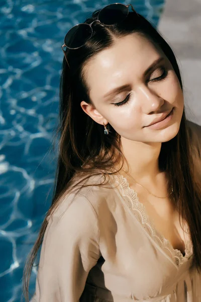 Modelo de menina bonita gosta do sol, os olhos estão fechados, em um fundo de água azul — Fotografia de Stock
