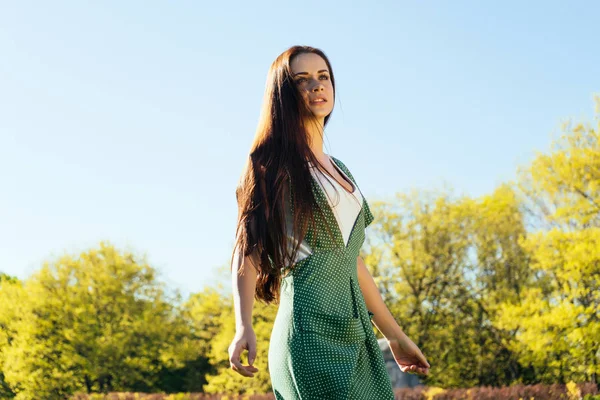 Fille rêveuse aux cheveux longs dans une robe verte profitant du temps chaud, marchant dans le parc — Photo