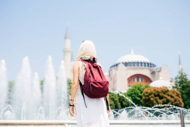 Bir eşarp ile cami ve Çeşme bir arka plan üzerine bir sırt çantası içinde tanınmayan bir kadın. Yaz tatili, gezgin