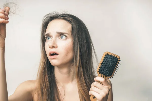 Jovem triste segurando um pente de madeira em suas mãos, perdendo o cabelo — Fotografia de Stock