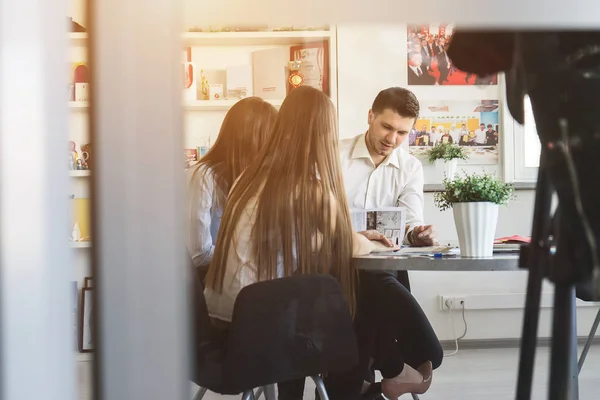 In un ufficio accogliente, due ragazze di successo e un ragazzo sono seduti a un tavolo e lavorano insieme su un progetto — Foto Stock