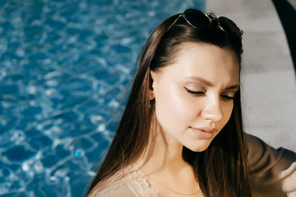 Modelo menina bonita nos raios do sol ofuscante, contra um fundo de água azul — Fotografia de Stock
