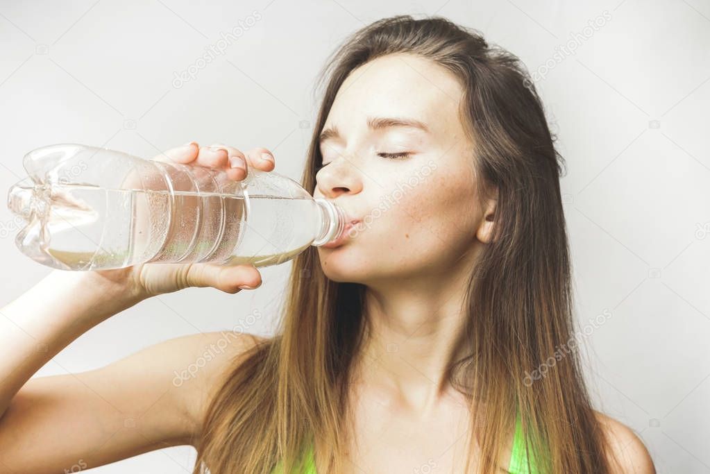 young beautiful girl drinks clean water from a plastic bottle after training, thirsty