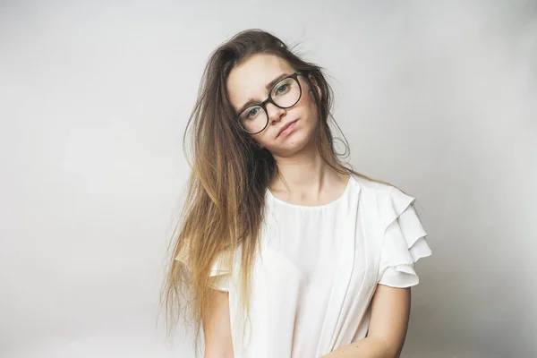 Muchacha joven pensativa con hermoso pelo largo, con una camiseta blanca y gafas, mirando a la cámara — Foto de Stock