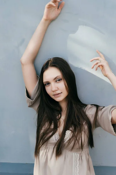 Sexy attractive model girl in beige dress posing on light background, hands raised upwards — Stock Photo, Image