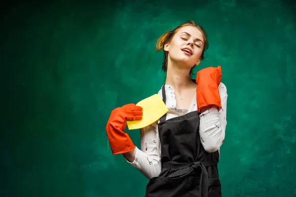 Beautiful young girl in a black apron, in rubber gloves holds a cleaning cloth — Stock Photo, Image