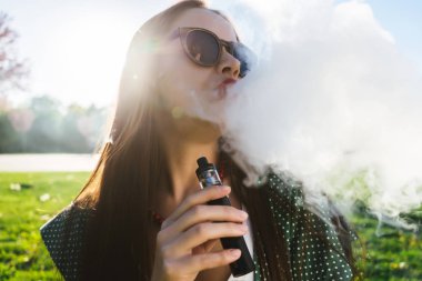 Mutlu moda gülümseyen kadın güneş gözlüğü vape Street, duman Sigara