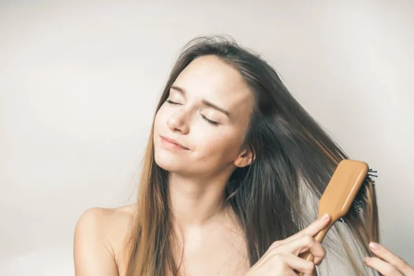 Sorrindo jovem penteando seu cabelo longo com um pente de madeira — Fotografia de Stock